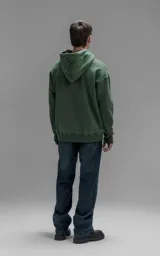 Hoodie oversize color verde, confeccionado en frisa premium con textura gamuzada. Presenta capucha ajustable con cordones personalizados, bolsillo frontal tipo canguro y puños con abertura para pulgar.