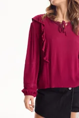 Blusa de viscosa color blanco con escote en V y cordón ajustable, mangas largas y volados decorativos en los hombros.