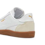 Championes Puma modelo Club 5V5, de diseño urbano inspirado en el fútbol sala. Presenta una base de cuero sintético blanco con refuerzos de gamuza en la puntera y el talón en tono beige, y una suela de goma color caramelo. Incluye el logo de la marca en dorado en el lateral y la lengüeta.