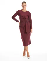 Vestido midi de seda fría color bordó, con cuello a la base, mangas largas y detalle de lazo ajustable en la cintura que crea un efecto drapeado lateral.