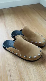 Zuecos color beige con tachas plateadas, base negra y plantilla con el logo de la marca.