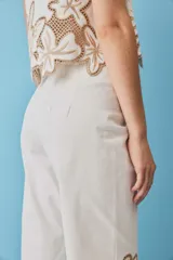 Pantalón negro de tiro alto y corte recto, confeccionado con detalles de bordados florales calados en la parte inferior de las piernas.