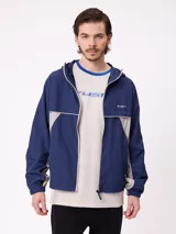 Rompevientos Rusty con capucha, diseño bicolor en azul marino y gris, cierre frontal y logo bordado en el pecho.