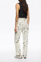 Pantalón de denim de corte recto y tiro alto, con diseño de cinco bolsillos y cierre frontal con botón y cremallera. Presenta un estampado de manchas oscuras sobre base de color terracota.