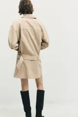 Vestido corto de cuello solapa y manga larga, con bolsillos delanteros y detalle de cinturón a tono. Presenta cierre frontal con cremallera oculta y bajo con aberturas laterales.