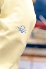 Buzo amarillo de corte holgado con mangas raglán en color azul, detalle de costuras acolchadas en los hombros y bordado de sol en el centro del pecho. Presenta puños y cuello acanalados con rayas azules.