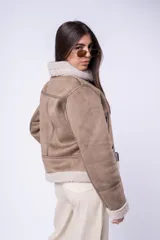 Campera tipo gamulán de corte recto, confeccionada en cuero sintético color tostado con interior y solapas de corderito sintético en tono crema. Presenta cierre frontal cruzado, bolsillos laterales con cierre y cinturón ajustable en el ruedo.