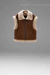 Chaleco marrón con cuello y borde de piel sintética color crema, cierre frontal con cremallera y bolsillos laterales.