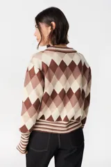 Sweater de punto con diseño de rombos en tonos marrones, beige y crema. Presenta cuello redondo, mangas largas con puños anchos acanalados y diseño de rayas en los puños y el ruedo.