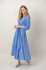 Vestido midi cruzado de seda con estampado de rayas celestes y blancas, escote en V con solapa, mangas tres cuartos y detalle de nudo drapeado en la cintura.