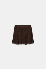 Falda corta de tiro medio confeccionada en tejido de encaje color marrón, con diseño evasé y detalle de aplicación de tachas metálicas en la cintura y el ruedo.