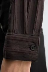 Camisa de manga larga con ajuste relajado, confeccionada en tejido de viscosa con textura de rayas verticales. Presenta cuello camisero, cierre frontal de botones y aberturas en el bajo lateral.