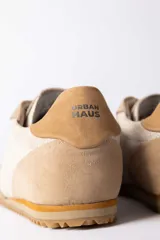 Championes urbanos de diseño retro, confeccionados en una combinación de gamuza y cuero texturizado en tonos beige y arena. Presentan cordones al tono y una suela dentada de goma en color caramelo.