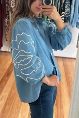 Camisa celeste de denim con bordado de hojas en las mangas, cuello con volados y botones de flor.