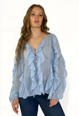 Camisa celeste de gasa con volados en el frente y mangas largas abullonadas.