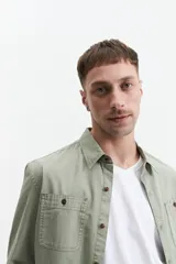 Camisa manga larga color verde oliva, corte slim fit, con cartera abotonada, dos bolsillos frontales con botón y confeccionada en 100% algodón.