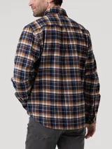 Camisa de manga larga de franela de algodón orgánico con estampado a cuadros en tonos azul marino, mostaza, blanco y marrón. Presenta cuello clásico, cierre frontal con botones de madera y dos bolsillos en el pecho.