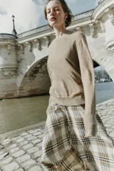 Falda midi de tiro alto con diseño asimétrico y estampado de cuadros en tonos beige, marrón y negro. Presenta una abertura frontal con acabados desflecados y cierre lateral con cremallera oculta.