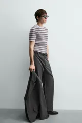 Pantalón de vestir gris oscuro, corte ancho (flare fit) y tiro alto, con bolsillos laterales y falsos bolsillos de vivo en la parte trasera. Presenta un cierre frontal con cremallera y gancho oculto, y botones a presión ocultos en el bajo.