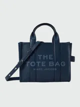 Cartera tipo tote de Marc Jacobs, confeccionada en cuero granulado color azul marino. Presenta el logo de la marca estampado en el frente, doble asa superior y correa ajustable y extraíble para llevar al hombro o cruzada.