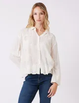 Camisa de algodón color gris con bordados florales en el frente y las mangas. Tiene cuello con solapa y cierre frontal con botones.