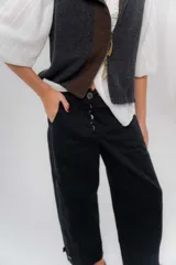 Pantalón de gabardina de algodón color negro, con calce barrel, cintura media baja, recortes de diseño y detalle de botones en el ruedo para ajustar el volumen.