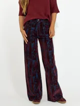 Pantalon de corte recto y tiro alto, confeccionado en denim con un acabado texturizado que combina tonos bordó y azul en un diseño abstracto. Presenta costuras verticales marcadas en el frente y bolsillos laterales.