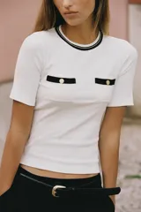 Camiseta negra de manga corta y corte slim fit, con cuello redondo ribeteado en blanco y dos bolsillos de plastrón en el pecho con un botón dorado cada uno.