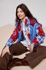 Campera de estilo camisa con diseño capitoneado y estampado patchwork que combina motivos florales, paisley y cuadros en tonos rojos y azules. Presenta cuello camisero, cierre frontal con botones y bolsillos delanteros.