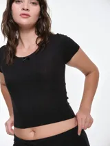 Remera de manga corta entallada en tejido pointelle, con escote redondo y detalle de picot con lazo pequeño en el centro. Diseño ajustado al cuerpo con textura acanalada.