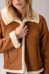 Campera tipo gamulán de cuero color tostado con interior y detalles en piel sintética color crema. Presenta cuello solapa, cierre frontal y mangas largas con puños de piel.