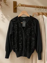 Cardigan negro de punto con frente decorado con lentejuelas brillantes. Presenta cuello redondo, cierre frontal con botones y mangas largas con puños ajustados.