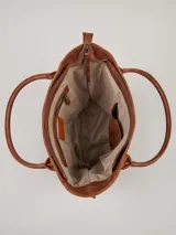 Cartera tipo tote bag de cuero vacuno marrón, con detalles de trenzado artesanal en los laterales y flecos colgantes decorativos. Cuenta con doble asa de hombro y cierre superior.