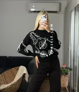 Sweater de tejido de punto con cuello redondo y diseño de bordado lineal en contraste que forma motivos orgánicos y florales. Presenta un corte clásico y mangas largas.