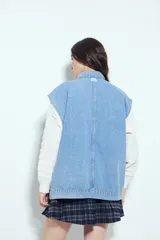 Chaleco de jean con corte oversized, diseño sin mangas, cuello camisero, cierre frontal con botones metálicos y bolsillos frontales tipo cargo.