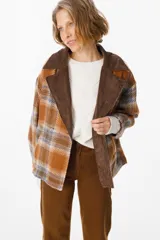 Blazer de corte holgado con diseño a cuadros en tonos naranja, azul y marrón. Presenta solapas anchas de pana en color marrón oscuro, cierre frontal cruzado con dos botones y bolsillos laterales integrados.