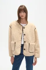 Campera de poliéster con textura de corderito en color beige, con cuello a la base y cierre frontal de botones. Presenta ribetes en contraste de color marrón oscuro en el cuello, la cartera, los hombros y en sus dos bolsillos frontales tipo parche.