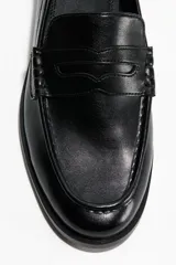 Mocasines estilo penny de color negro, con costura tradicional en la parte delantera y suela baja.