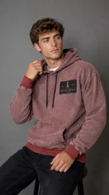 Hoodie de algodón con efecto lavado, color bordó, con capucha, cordones negros ajustables, bolsillo frontal tipo canguro y parche rectangular con logo de la marca en el pecho.