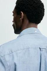 Camisa de corte regular fit confeccionada en tejido chambray de algodón con efecto lavado. Presenta cuello con botones, manga larga con puños abotonados, bolsillo en el pecho y cierre frontal de botones.