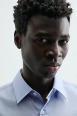 Camisa de manga larga, color blanco, con cuello italiano y corte slim fit. Presenta cierre frontal de botonadura y puños con botón.