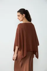 Poncho corto de tejido de punto color habano con sutiles destellos brillantes, de cuello bote y mangas amplias.