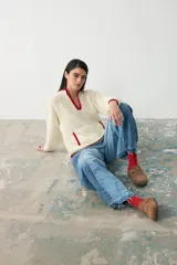 Sweater de tejido bouclé color crudo con detalles de ribete en color rojo en el cuello, puños y bolsillos. Presenta un diseño de manga larga, cuello en V y bolsillos frontales.