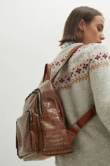 Mochila de cuero sintético con textura croco color marrón chocolate, con cierre principal y bolsillo frontal con cierre. Cuenta con tirantes ajustables y asa superior.