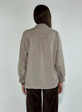 Camisa color beige con cuello mao, mangas largas abullonadas y cierre frontal con botones.