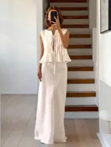 Conjunto de top y falda color crema, confeccionado en lino. El top es sin mangas, con detalle de lazos en el escote y volados en el ruedo. La falda es larga y de corte recto.