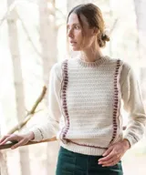 Sweater artesanal tejido a mano en lana merino, de color marfil con detalles en bordó. Presenta cuerpo delantero en crochet con guardas laterales decorativas y espalda en punto jersey, con cuello redondo y puños acanalados en contraste de color.