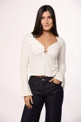 Blusa de algodón color blanco, con escote en V y detalle de argolla metálica en el centro. Presenta mangas largas con terminación oxford acampanada y ruedo con terminación ondulada.