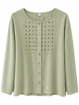Camisa de manga larga color verde menta con cuello redondo y cierre frontal de botones. Presenta un panel rectangular de broderie con detalles geométricos perforados en el pecho.
