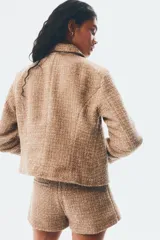 Chaqueta corta de tejido texturizado en color tostado, con cuello camisero, cierre frontal de botones metálicos dorados y diseño entallado con costuras moldeadoras.